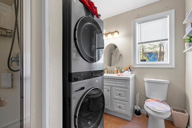 bathroom featuring vanity, stacked washer and dryer, toilet, and tile patterned flooring