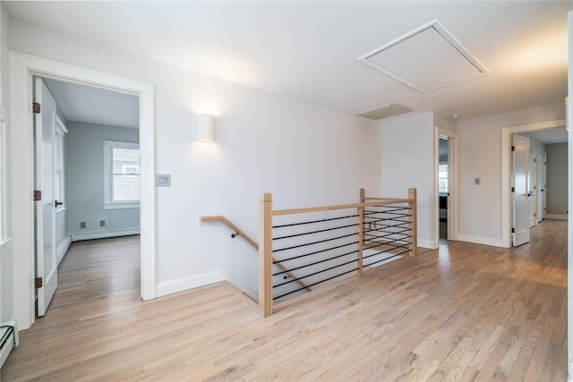 empty room featuring a baseboard heating unit, light wood finished floors, attic access, and baseboards