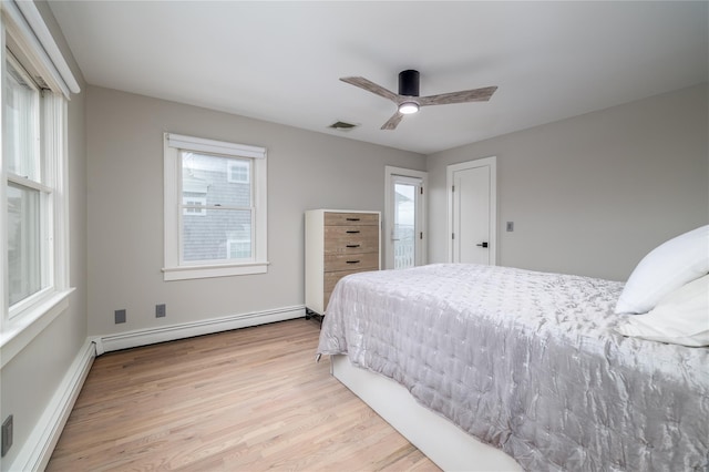 bedroom featuring a baseboard heating unit, light wood finished floors, multiple windows, and visible vents