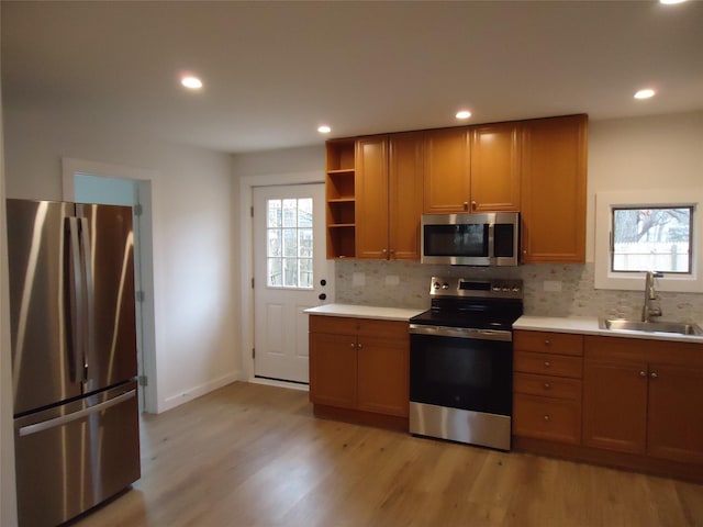 kitchen with a sink, stainless steel appliances, light wood finished floors, decorative backsplash, and a healthy amount of sunlight