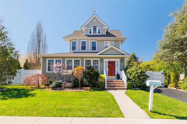 view of front facade featuring roof with shingles, a front yard, and fence