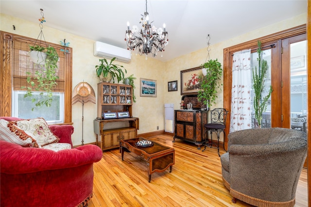 living area with baseboards, an AC wall unit, wood finished floors, and an inviting chandelier