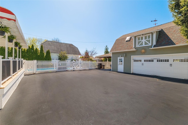 exterior space with a garage, roof with shingles, fence, and an outbuilding