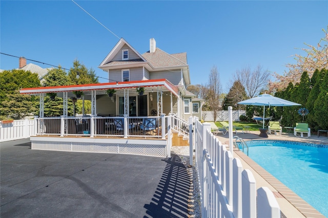 rear view of property with a fenced in pool, a chimney, covered porch, fence, and a patio area