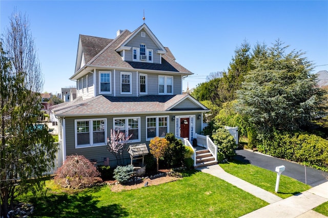 american foursquare style home with a shingled roof, a front yard, and fence