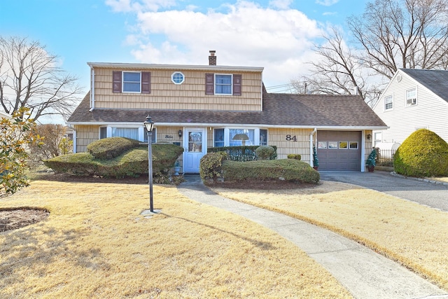 view of front of house with a front yard, roof with shingles, driveway, an attached garage, and a chimney