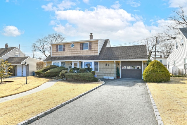 view of front of house featuring driveway, a front yard, a shingled roof, a garage, and a chimney