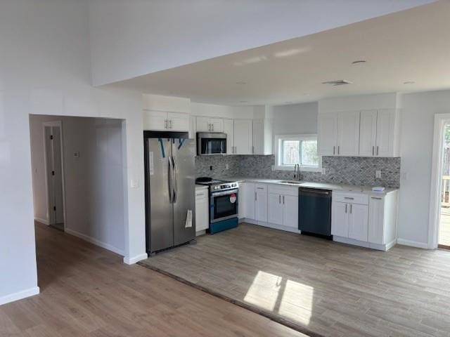 kitchen with stainless steel appliances, light countertops, decorative backsplash, white cabinetry, and a sink