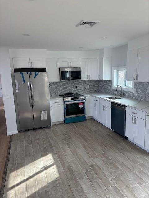 kitchen featuring visible vents, light wood-style flooring, a sink, stainless steel appliances, and backsplash