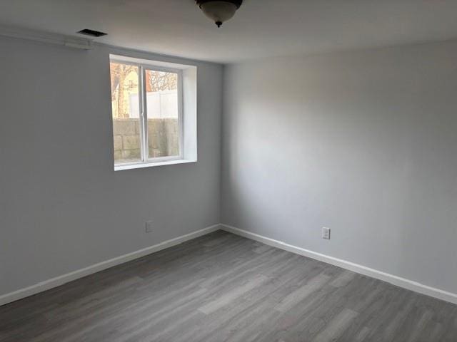 empty room featuring dark wood-style flooring, visible vents, and baseboards