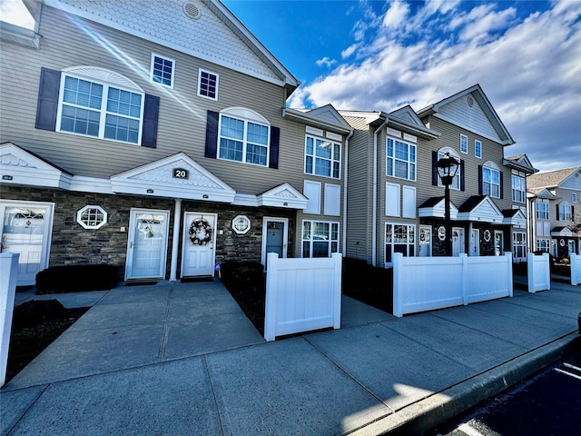 view of property with stone siding, a residential view, and fence