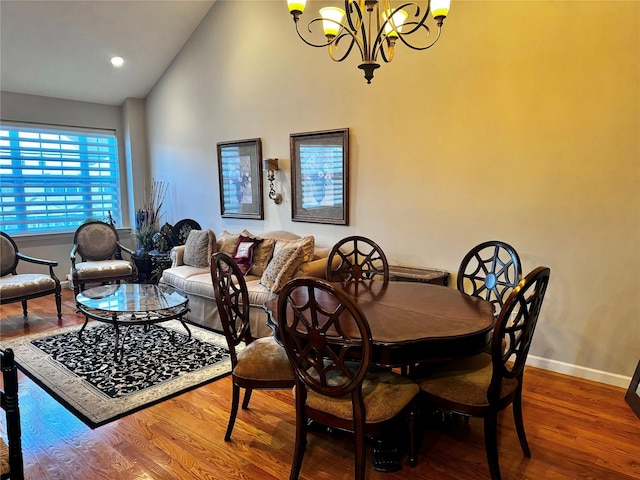 dining area featuring lofted ceiling, baseboards, wood finished floors, and a notable chandelier