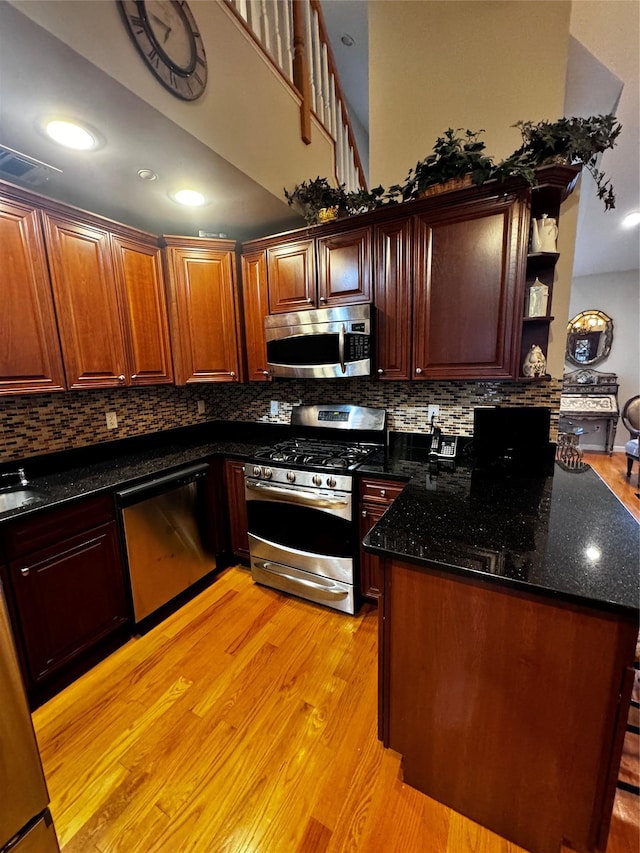 kitchen featuring light wood finished floors, open shelves, decorative backsplash, appliances with stainless steel finishes, and a peninsula