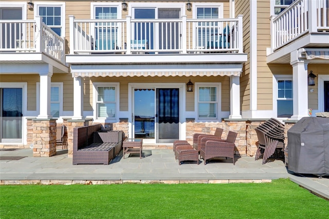 rear view of property featuring an outdoor hangout area, a patio, stone siding, and a balcony