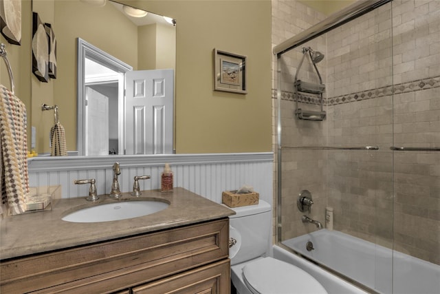 bathroom featuring toilet, wainscoting, enclosed tub / shower combo, and vanity