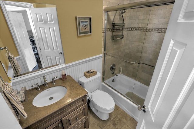 bathroom featuring toilet, enclosed tub / shower combo, vanity, and wainscoting