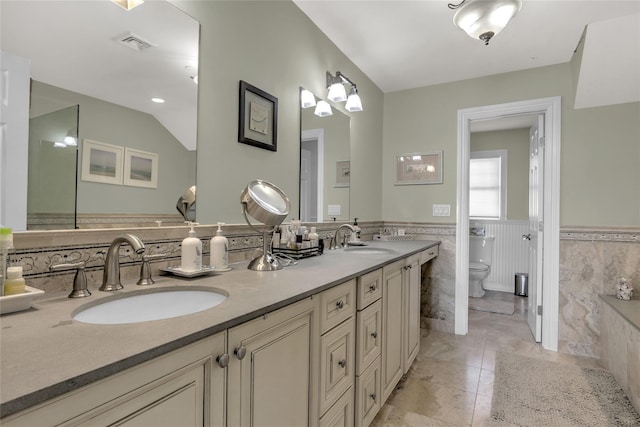 full bathroom with a wainscoted wall, a sink, toilet, and double vanity