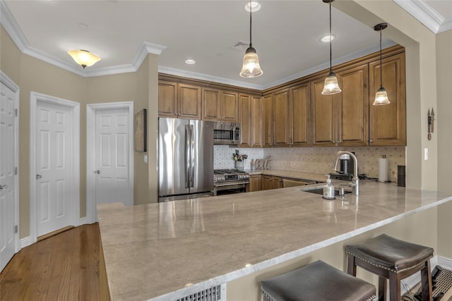 kitchen with appliances with stainless steel finishes, brown cabinetry, ornamental molding, a sink, and a peninsula