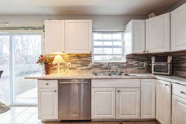 kitchen with light tile patterned floors, a sink, white cabinets, backsplash, and dishwasher