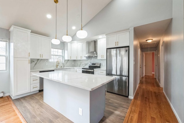 kitchen with lofted ceiling, appliances with stainless steel finishes, a sink, wall chimney range hood, and a kitchen island