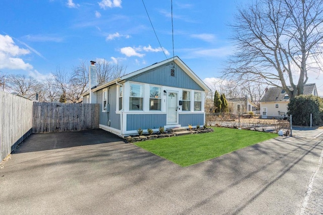 bungalow-style house with aphalt driveway, a chimney, a front yard, entry steps, and fence