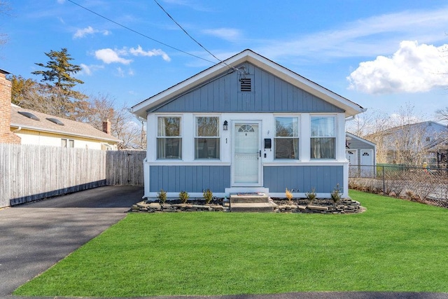 bungalow-style house featuring aphalt driveway, a front yard, and fence