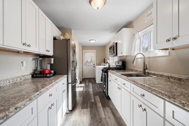 kitchen with dark wood-style flooring, stainless steel appliances, white cabinets, a sink, and separate washer and dryer