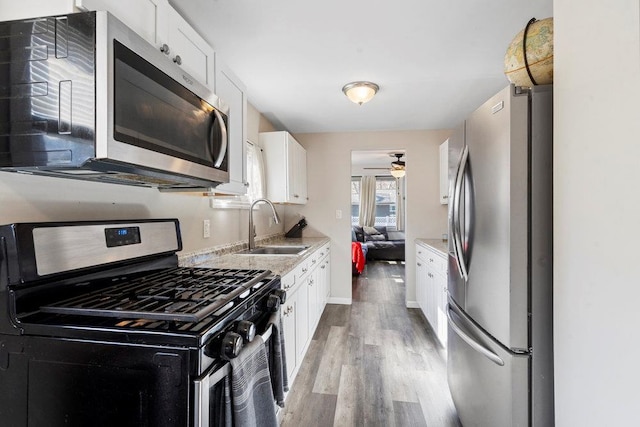 kitchen featuring appliances with stainless steel finishes, white cabinets, a sink, ceiling fan, and light wood-type flooring