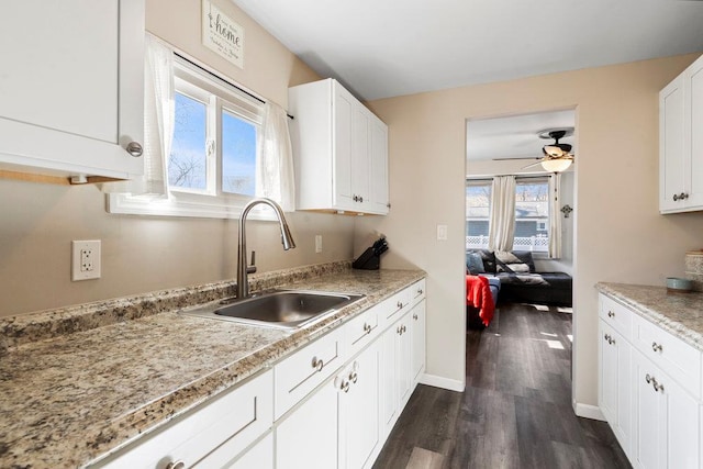 kitchen featuring dark wood-type flooring, white cabinets, a sink, and baseboards