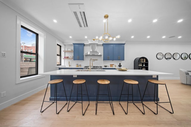 kitchen featuring a kitchen bar, blue cabinetry, light countertops, and wall chimney range hood