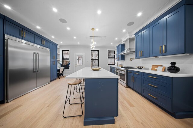 kitchen with blue cabinetry, wall chimney range hood, light countertops, a kitchen bar, and premium appliances