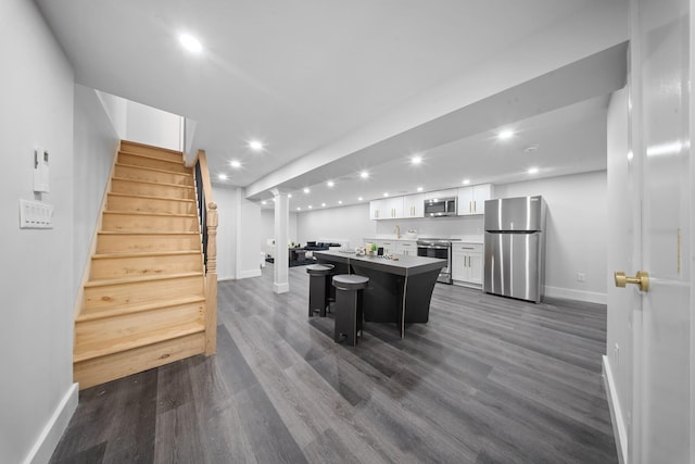 kitchen with a kitchen island, dark wood finished floors, stainless steel appliances, white cabinets, and a kitchen bar