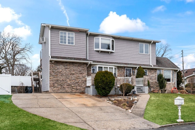 view of front of property with stone siding, fence, a front lawn, and concrete driveway