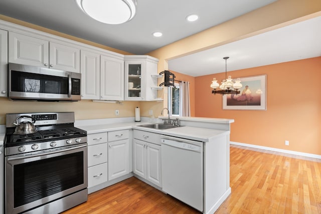 kitchen featuring stainless steel appliances, light countertops, light wood-style flooring, a sink, and a peninsula