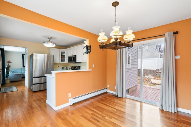 kitchen with appliances with stainless steel finishes, glass insert cabinets, a peninsula, a baseboard heating unit, and white cabinetry