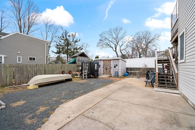 view of patio with a fenced backyard, an outdoor structure, a storage shed, and stairs