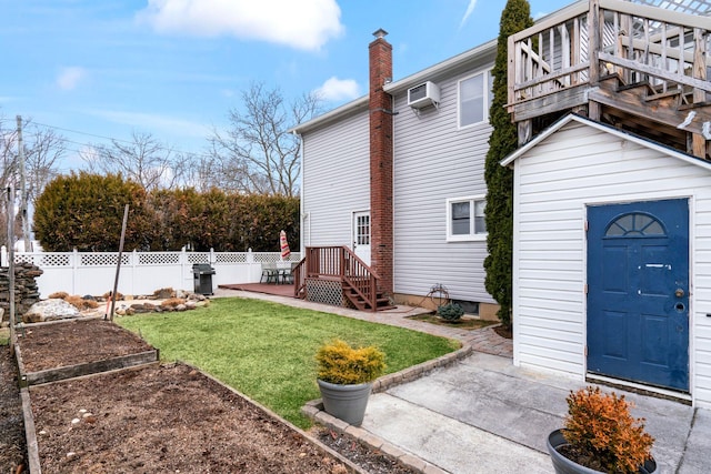 exterior space with a vegetable garden, a wall unit AC, an outbuilding, fence, and a wooden deck