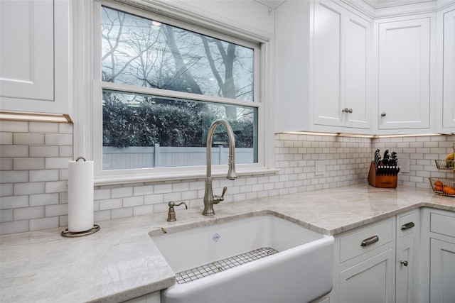 kitchen with light stone counters, a sink, white cabinetry, and decorative backsplash