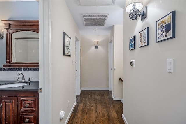 corridor with dark wood-style flooring, a sink, visible vents, baseboards, and attic access