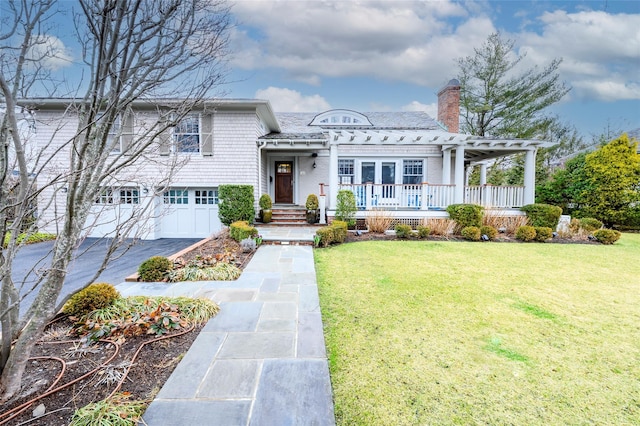 view of front of property with a porch, a garage, driveway, a chimney, and a front yard