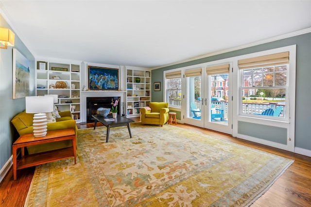 living area with baseboards, a fireplace with flush hearth, wood finished floors, crown molding, and french doors