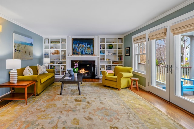 living area with baseboards, a lit fireplace, ornamental molding, and wood finished floors