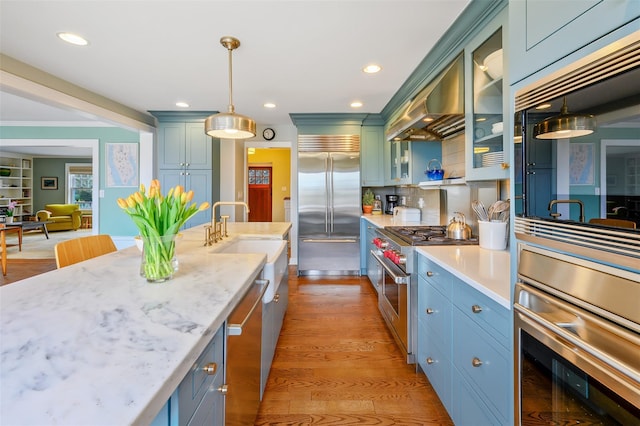 kitchen featuring hanging light fixtures, light wood finished floors, wall chimney exhaust hood, and high end appliances