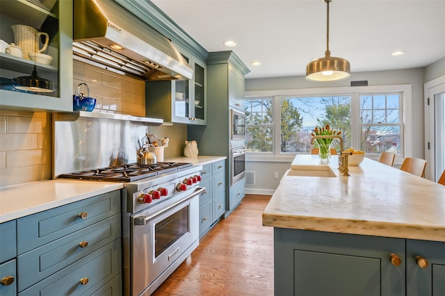 kitchen with stainless steel appliances, light countertops, range hood, tasteful backsplash, and green cabinetry