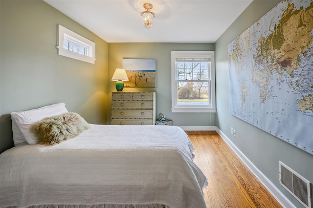 bedroom featuring baseboards, multiple windows, visible vents, and wood finished floors