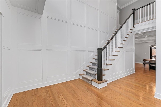 staircase with crown molding, wood finished floors, and a decorative wall