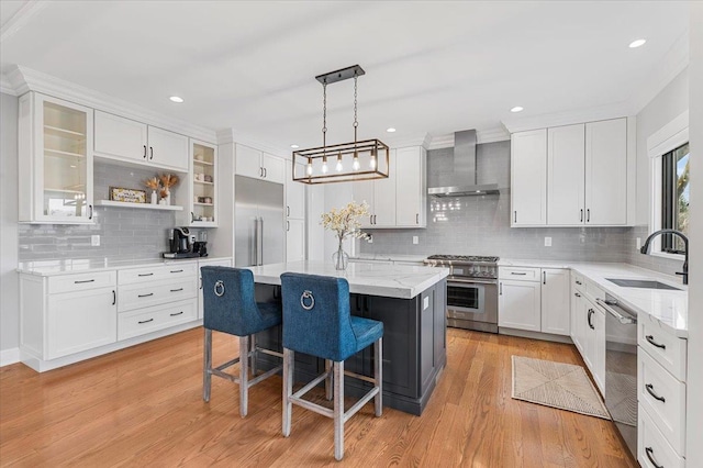 kitchen with wall chimney exhaust hood, high end appliances, a sink, a kitchen island, and a kitchen breakfast bar