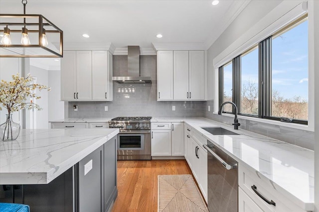 kitchen featuring stainless steel appliances, a sink, light wood-style floors, wall chimney exhaust hood, and crown molding