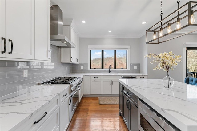 kitchen featuring tasteful backsplash, wall chimney exhaust hood, appliances with stainless steel finishes, light wood-type flooring, and a sink