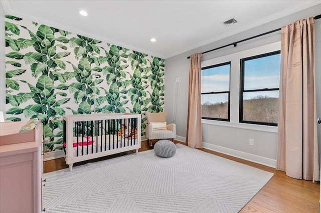 bedroom featuring wallpapered walls, baseboards, an accent wall, ornamental molding, and light wood-type flooring